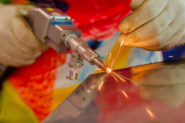 Close up: welder hands using portable handheld laser welding machine with sparks. Manufacturing, industrial, equipment, technology and metalworking concept - Powered by Adobe
