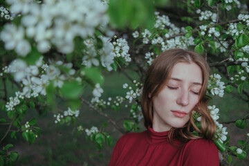a blonde girl in red unites with nature in a garden of flowering trees