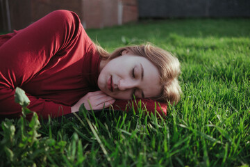 a blonde girl in red lies on the grass in the summer and enjoys the weather