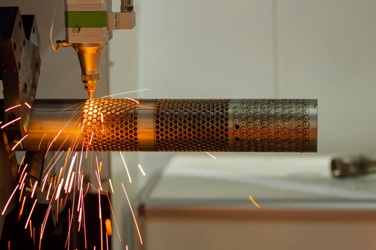 CNC laser cutting machine working with cylindrical metal workpiece with many sparks at factory, plant. Metalworking, industrial, manufacturing, technology and equipment concept