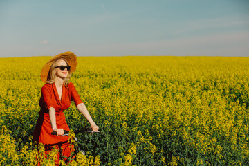  girl in vintage dress and sunglasses with bicycle in rapeseed field