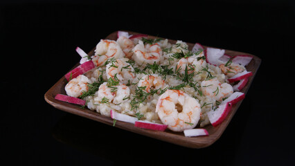 homemade brown rice dish with shrimps with radishes and herbs served on a wooden plate in the dark