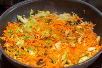Homemade cooking. A woman fries onions and carrots in a hot frying pan with vegetable oil.