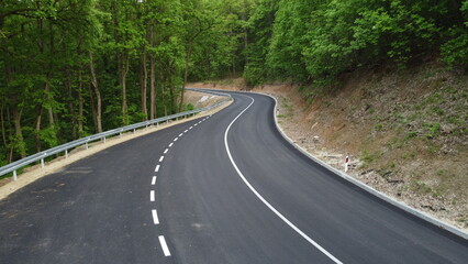 Aerial shot of a winding road passing through a beautiful dense green forest	