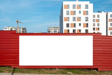 Blank white advertising banner on the fence of construction site. Residential area with modern buildings on a sunny day. © diesirae