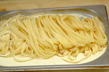 The pasta, cut into long strips, lies on a wooden tray. Use your hands to stir the raw pasta for cooking.