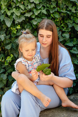 Joyful older sister holding younger sister, playing and laughing, having fun. Teen girl holding baby girl on summer day. Children with large age gap. Big age difference between siblings