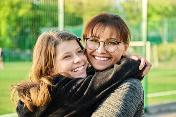 Portrait of happy mom and preteen daughter hugging together outdoor