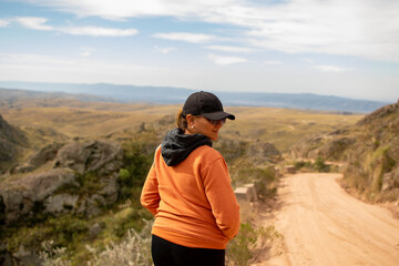 Portrait of latin woman dressed in orange with a cap and tail turned back having fun during the day of trekking in the mountain forest - Focus from the back