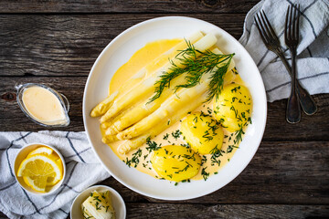 White boiled asparagus in hollandaise sauce with potato puree served on wooden black table
