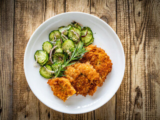 Breaded fried pork chop with sliced cucumbers and rosemary on wooden table
