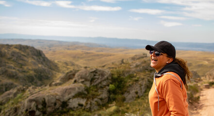 Naklejka premium Portrait of latin woman dressed in orange with a cap and tail in the back having fun during the day of trekking in the mountain forest - laughing out loud