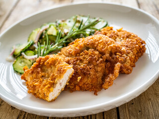 Breaded fried pork chop with sliced cucumbers and rosemary on wooden table
