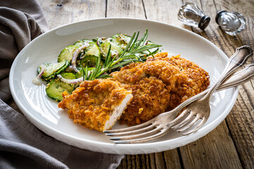 Breaded fried pork chop with sliced cucumbers and rosemary on wooden table
