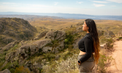 Fototapeta premium Portrait of Latin woman dressed in black with a cap having fun during the day of trekking in the mountain forest - looking at the horizon
