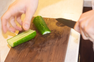 Preparation of vegetable salad. Close-up of a man's hand with a knife chopped cucumber