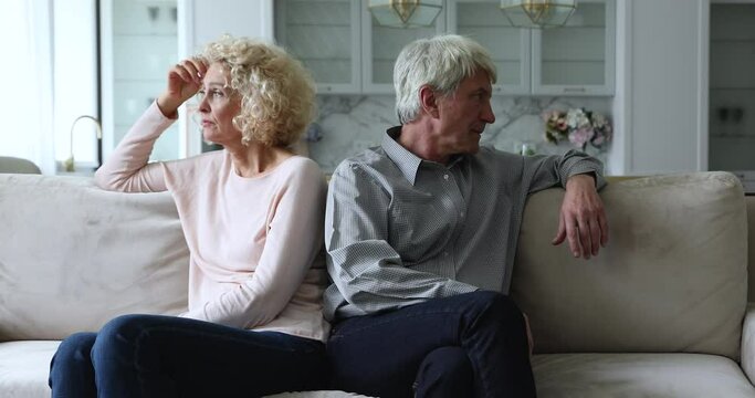 Mature sad couple sit separate on couch ignoring each other, avoid talking after fight, having misunderstandings, experiencing relationship crisis, think of break up or divorce. Marriage split concept