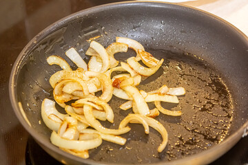 Close up of sauteed onion and garlic in the frying pan. Man preparing dinner. Cooking at home concept. Selective focus.