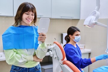 Teenage female looking at healthy teeth in mirror, in dental office