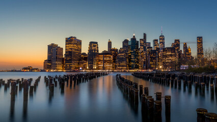 Fototapeta na wymiar New York, USA - April 25, 2022: Long exposure of the Lower Manhattan skyline at sunset with an old Brooklyn pier in the foreground