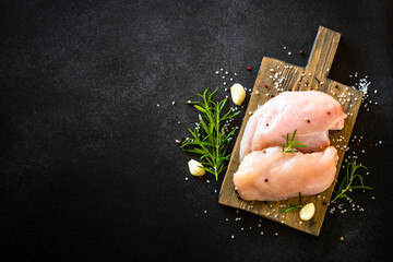 Chicken fillet with ingredients at wooden board at black stone table. Top view with copy space.