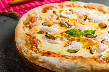 Pizza with seafood, shrimps and squid with cheese on wooden board on grey table