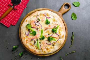 Pizza with salmon and broccoli on wooden board on grey table top view