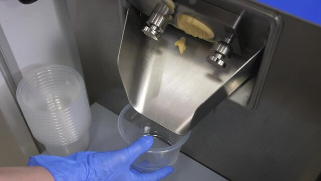 Industrial preparation of italian creamy ice cream. The worker's hand substitutes a plastic container for filling it with banana, vanilla and mango flavored ice cream.
