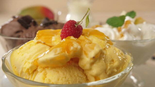 Three glass bowls filled with ice cream balls with flavors of ice cream, chocolate, mango and banana are spinning in front of the camera. Stops at white ice cream.