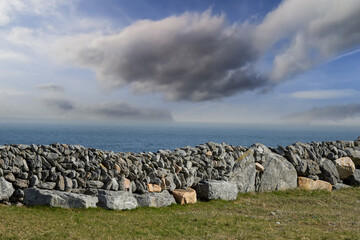 Traditional stone fences or walls in foreground, cloudy sky and blue ocean in background....