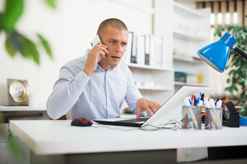Naklejka premium Portrait of focused manager sitting at office table, having phone conversation