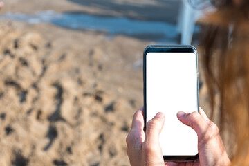 Person holding a smartphone on the beach with a blank screen.