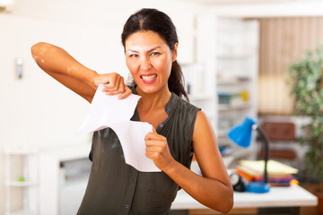 Desperate aggressive business woman ripping paper documents in modern office