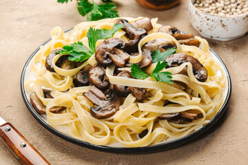 Delicious pasta with champignon mushrooms on plate with parsley on beige stone kitchen table background, top view. Healthy vegan cooking and eating. Italian food concept