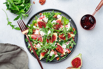 Delicious summer salad with sweet  figs, white feta cheese, walnuts, arugula and jam vinegar dressing on white table background, top view, negative space - obrazy, fototapety, plakaty