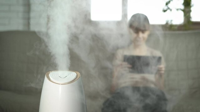 Girl working by air purifier. A teen sits on the sofa with her ipad by the smart air purifier in the living room.