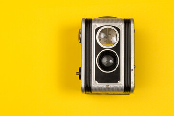 Old stylish vintage dual lens camera on yellow background with copy space. Leather and metal rangefinder retro camera with film, memories and nostalgia background. Photography course and training add