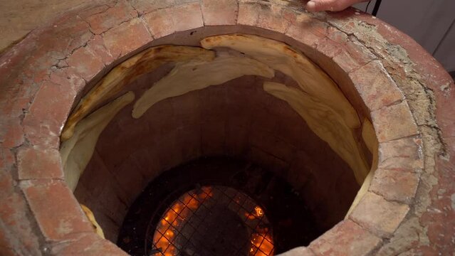 Tandoor. Inside oven, fire burns and flat bread is baked on walls. Khachapuri. Georgian cuisine. Bakery or bakery production. man glues bread to wall. Georgian cuisine.