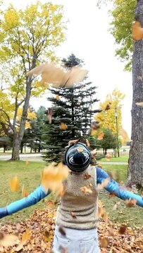 Throw Your Hands Up in the Air it's Fall!  Middle age caucasian female throws autumn leaves up in the air in slow motion. Wearing hat and vest with back to camera. 