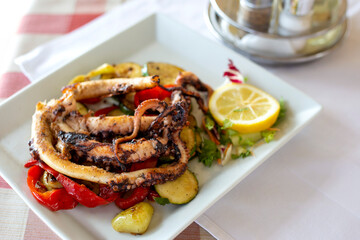 Grilled octopus with lemon and grilled zucchini in white plate on the table