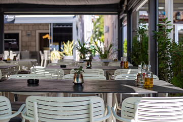 Empty mediterranean street cafe with white chairs and black tables
