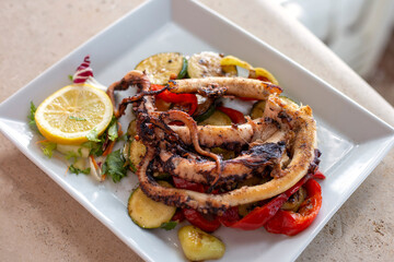 Grilled octopus with lemon and grilled zucchini in white plate