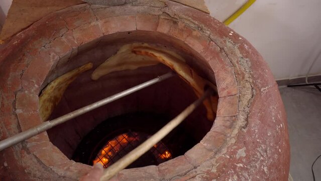 Tandoor. Inside oven, fire burns and flat bread is baked on walls. Khachapuri. Georgian cuisine. Bakery or bakery production. man with stick takes bread from wall of oven.