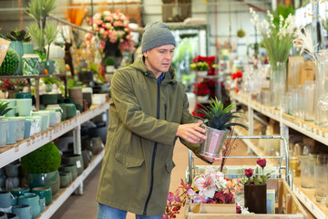 Male customer in winter clothes chooses cactus flower in flower shop