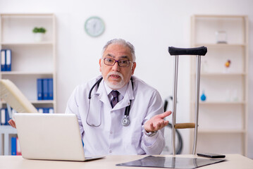 Leg injured old male doctor working in the clinic