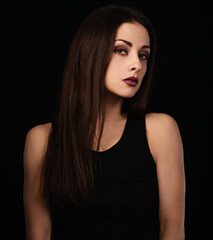Fototapeta premium Beautiful bright makeup woman with red lipstick in black top and long brown healthy hair looking on dark black shadow background. Closeup