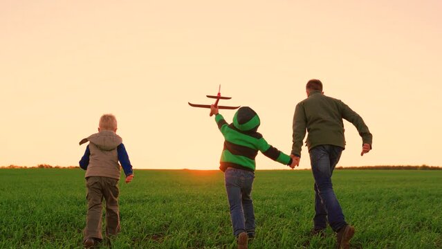 Carefree kids with toys playing outdoors. Children, boys run with toy plane in hand springfield in rays of sunset. Boy's group dreams of flying. Happy child runs in park, playing with toy airplane.