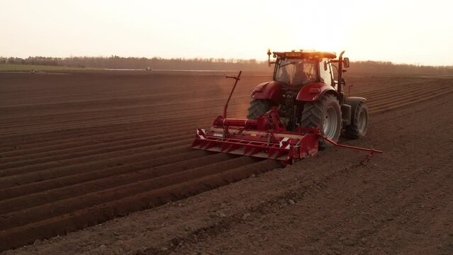 Contemporary tractor drags plug making furrows on soil in field at sunlight. Start of the planting season and sowing wheat. Avoiding a food crisis concept. April 2022, Prague, Czech Republic