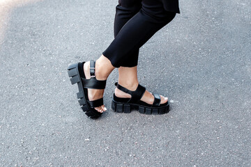 Female legs in blak fashion and stylish boots with beautiful pedicure nails on grey road background