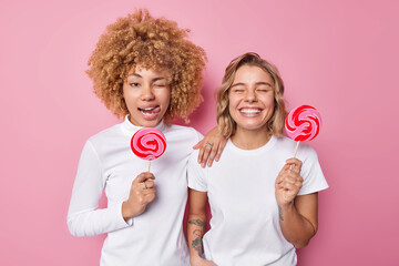Two playful young women smile gladfully wink eyes and stick out tongue foolish around dressed in...